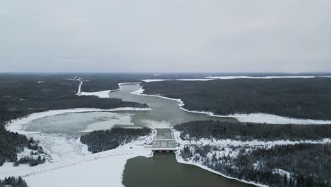 Drones-De-Gran-Altitud-Extrema-En-Una-Larga-Carretera-Cubierta-De-Nieve-Con-Agua-Corriendo-Por-La-Presa-Hidroeléctrica-De-Notigi-En-El-ártico