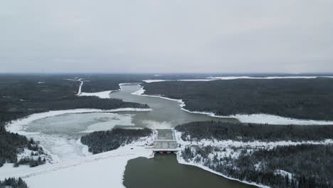 Extreme-High-Altitude-Drone-Out-Long-Snow-Covered-Road-with-Rushing-Water-Notigi-Hydroelectric-Dam-in-the-Arctic