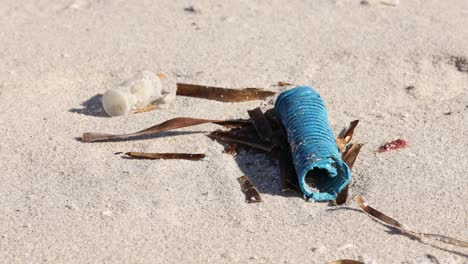 Primer-Plano-De-Un-Objeto-De-Plástico-Azul-Desechado-En-Una-Playa-De-Arena,-Concepto-De-Contaminación-Ambiental