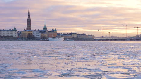 Gamla-Stan-and-Slussbron-against-sunset-sky,-tracking-shot-over-frozen-water