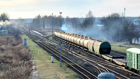 Freight-train-carrying-tankers-on-railway-with-industrial-backdrop,-daytime