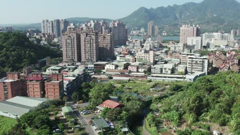 Drone-Sobrevolando-Edificios-Y-Parques-En-Zhuwei,-Distrito-De-Tamsui,-Taipei