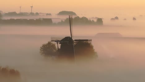 Aerial-view-of-traditional-old-windmill-in-a-meadow-with-low-fog-at-sunrise,-Friesland,-Netherlands