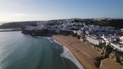 Panoramic-Aerial-of-Wide-Sandy-beach-with-gentle-rolling-waves-and-white-condo-homes-of-Albufeira-Portugal