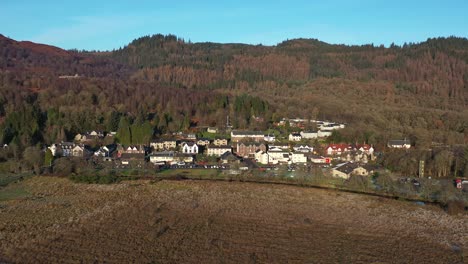 Malerische-Luftaufnahme-über-Die-Felder-Mit-Blick-Auf-Das-Dorf-Aberfoyle-Und-Den-Hügelhintergrund-In-Schottland-Im-Herbst-An-Einem-Sonnigen-Tag