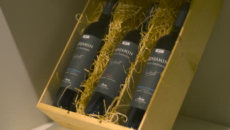 Exclusive-red-wine-bottles-lying-in-hay-in-open-wooden-box,-Benjamin