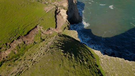 Immersive-tilt-down-aerial-view-of-some-cliffs-with-birds-flying-around-on-a-sunny-day,-Cucao-Chiloe-Chile
