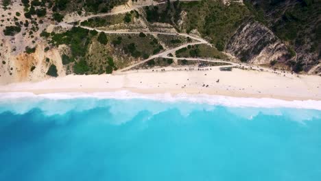 Myrtos-Strand-Auf-Kefalonia,-Griechenland-Mit-Türkisfarbenem-Wasser-Und-Sandstrand,-Touristen-Entspannen,-Luftaufnahme