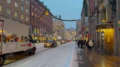 Snowy-evening-with-Christmas-lights-on-Stockholm's-Kungsgatan,-busy-with-pedestrians-and-traffic