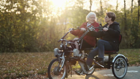 Elderly-mother-with-mature-daughter-on-special-mobility-scooter-bicycle-for-two