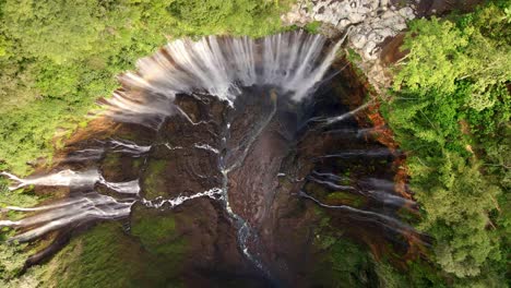 the-awe-inspiring-Tumpak-Sewu-Waterfall-from-above-in-this-aeria-4k-drone-footage,-capturing-its-grandeur-as-it-cascades-down-steep-cliffs-amidst-lush-greenery