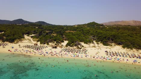 Cala-agulla-beach-with-crowds-enjoying-the-sun-and-clear-waters,-summer-vibe,-aerial-view