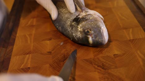 Chef-Skilfully-Slicing-Around-Fish-Head-On-Wooden-Chopping-Board