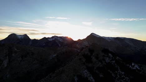 Vista-Aérea-Panorámica-Mientras-El-Sol-Se-Extiende-A-Través-De-Los-Picos-Montañosos-De-Agrafa-Grecia,-Telón-De-Fondo-Natural