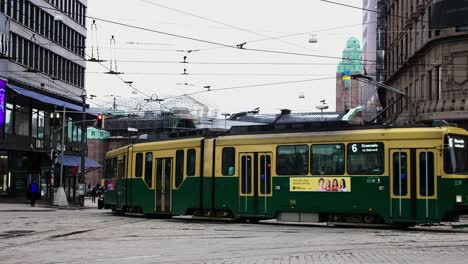 Green-trams-navigate-a-busy-Helsinki-street-on-a-cloudy-day,-city-vibe