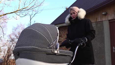 Mother-with-baby-carriage-stand-in-windy-countryside-environment-near-cottage