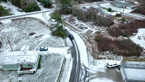 Drone-shot-of-car-driving-through-a-snow-covered-neighborhood