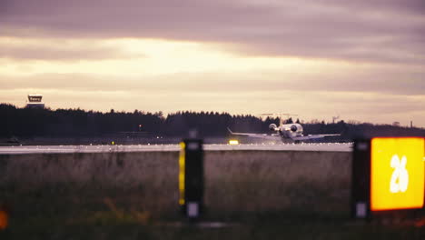 Bombardier-CRJ-900-landing-on-Tallinn-airport-runway-in-red-sunset-with-taxiway-signs-and-runway-warning-lights-in-foreground