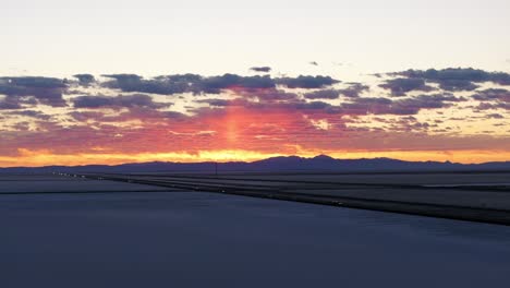 Cars-driving-at-sunset-along-highway-crossing-Bonneville-Salt-Flats-in-Utah,-USA