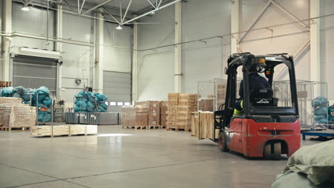 Slow-motion-of-warehouse-worker-operating-a-red-forklift-with-load-inside-a-new-warehouse-full-of-boxes-in-airport-hangar