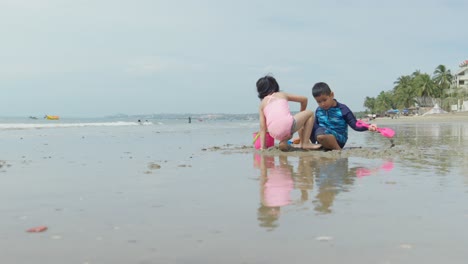 Dos-Niños-Asiáticos-Jugando-En-La-Arena-De-Una-Hermosa-Playa
