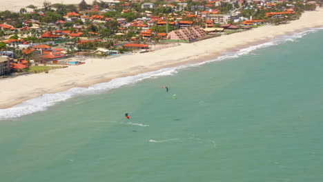 Aerial-view-of-people-practing-kite-surf-and-a-small-village-around,-Cumbuco,-Ceara,-Brazil
