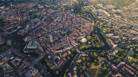 Sunrise-aerial-view-of-Amsterdam-with-historic-buildings,-canals,-and-vivid-urban-green-spaces