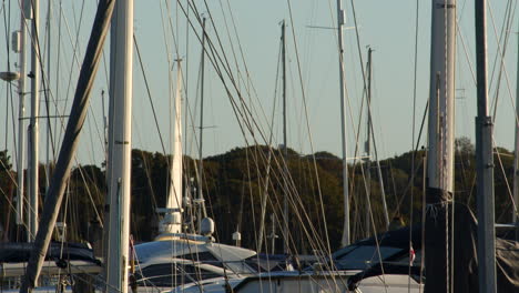 Aufnahme-Von-Yachtmasten-Im-Hafen-Von-Lymington-Mit-Vorbeisegelndem-Boot-Im-Hintergrund-In-Der-Marina-Von-Lymington