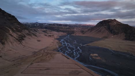 Aerial-landscape-view-of-a-river-flowing-in-a-mountain-valley,-in-Iceland,-on-a-cloudy-day