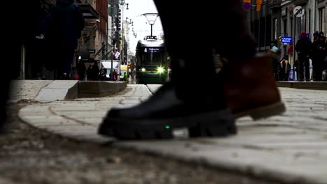 Low-angle-view-of-Helsinki-street-with-tram,-people,-and-cars-on-cobblestone,-cloudy-day