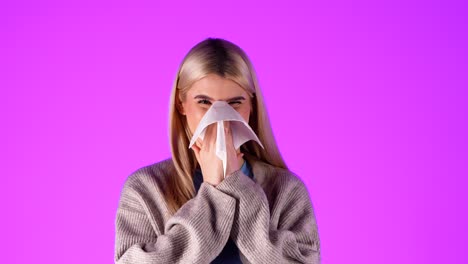 Portrait-Shot-of-caucasian-blonde-young-woman-sneezing-and-blowing-her-nose-at-infinite-magenta-studio-chroma-background