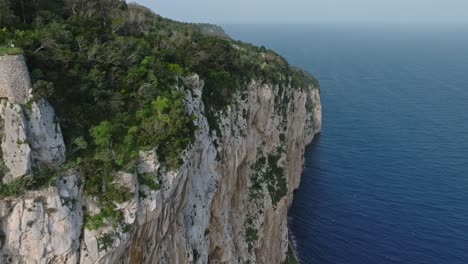 Aerial-shot-of-ancient-ruins-on-Capri's-steep-cliffs-overlooking-the-blue-sea
