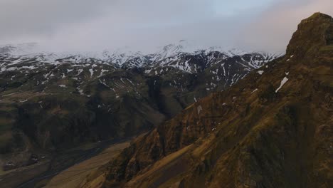 Vista-Aérea-Del-Paisaje-De-Un-Río-Que-Fluye-En-Un-Valle-De-Montaña,-Bajando-De-La-Nieve-Derretida,-En-Islandia,-En-Un-Día-De-Mal-Humor