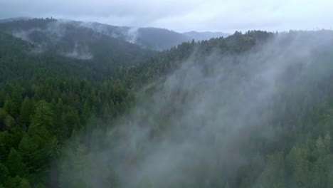 Toma-Brumosa-En-Cámara-Lenta-De-Niebla-Verde-Y-Profundo-Pico-De-Montaña-Paisaje-Tormentoso-Rayos-De-Sol-Que-Llegan,-Vista-Aérea-De-Drones