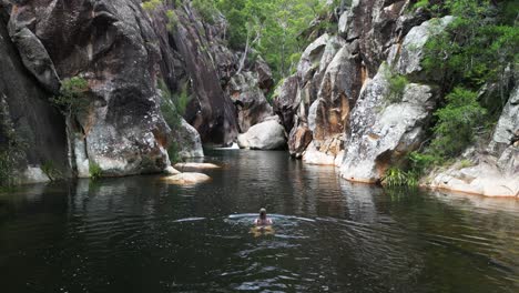 A-female-tourist-swims-in-a-secluded-Australian-waterhole-surrounded-by-towering-walls-of-coloured-sandstone