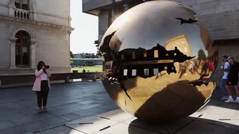 Young-woman-frames-the-Sphere-within-Sphere-bronze-sculpture-at-Dublin-Trinity-College