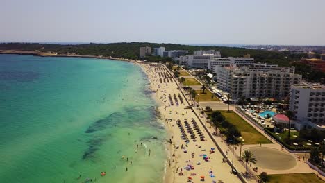 Cala-major-beach-with-turquoise-waters-and-sunbathers,-sunny-day,-aerial-view