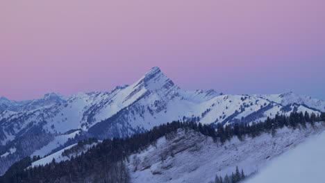 Cautivadora-Vista-Aérea-Que-Muestra-La-Tranquila-Silueta-De-Una-Cadena-Montañosa-Cubierta-De-Nieve-Al-Amanecer,-Filmada-Con-Un-Dron