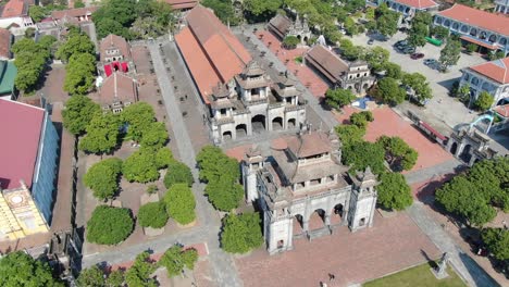 Drone-aerial-view-in-Vietnam-circling-around-over-a-stone-temple-in-Ninh-Binh-on-a-town-with-brick-roof-buildings-on-a-sunny-day