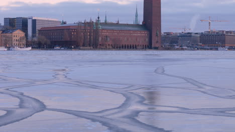 Stockholm-City-Hall-sunset-aerial-reveal-over-frozen-Riddarfjärden,-Sweden