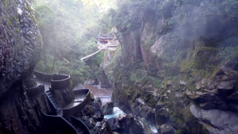 Misty-view-of-Baños'-waterfalls-and-natural-pools-with-a-spiraling-staircase,-enveloped-in-lush-greenery