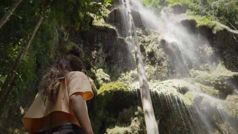 Tilt-up-to-woman-in-crop-top-looking-at-cascading-mist-of-water-falling-in-tropical-jungle