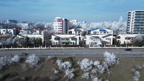 Vehicles-Driving-In-The-Road-Passing-By-On-Buildings-And-Trees-Covered-In-Ice-At-Winter-In-Galati,-Romania