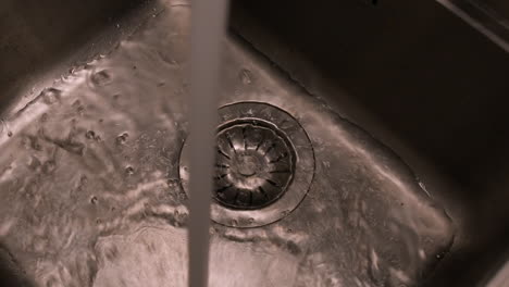 Close-up-detail:-Stream-of-water-flows-from-tap-in-steel-kitchen-sink
