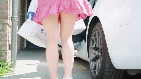 Girl-with-short-pink-skirt-opening-Tesla-door-and-grabbing-filled-grocery-bags