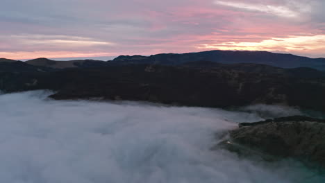 Misty-mountains-at-dawn-with-soft-pink-skies,-aerial-view