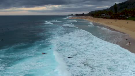 Vista-Aérea-De-Las-Olas-Rompiendo-Sobre-Los-Surfistas-En-La-Orilla-Del-Parque-De-La-Playa-Ehukai,-Ohau