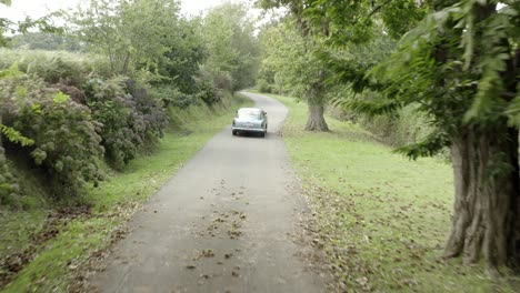 Vintage-car-driving-along-countryside-rural-road