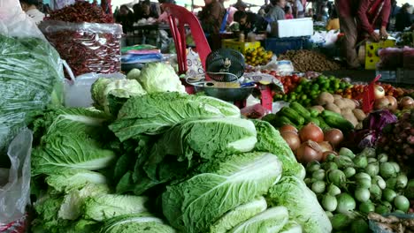 A-close-up-view-showcases-an-assortment-of-green-leafy-and-vibrant-non-leafy-vegetables,-with-unidentifiable-individuals-visible-in-the-background