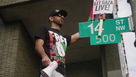 An-Arab-Man-in-a-Free-Palestine-Shirt-Holding-a-Ceasefire-Sign-on-Top-of-a-Street-Sign-at-the-March-on-Washington